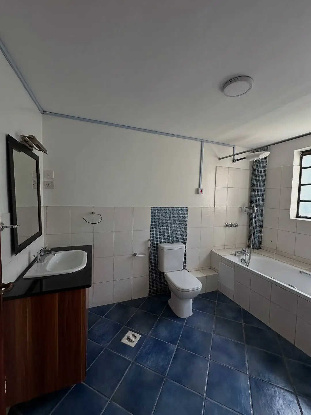Spacious bathroom with bathtub, toilet, sink, and blue tile flooring