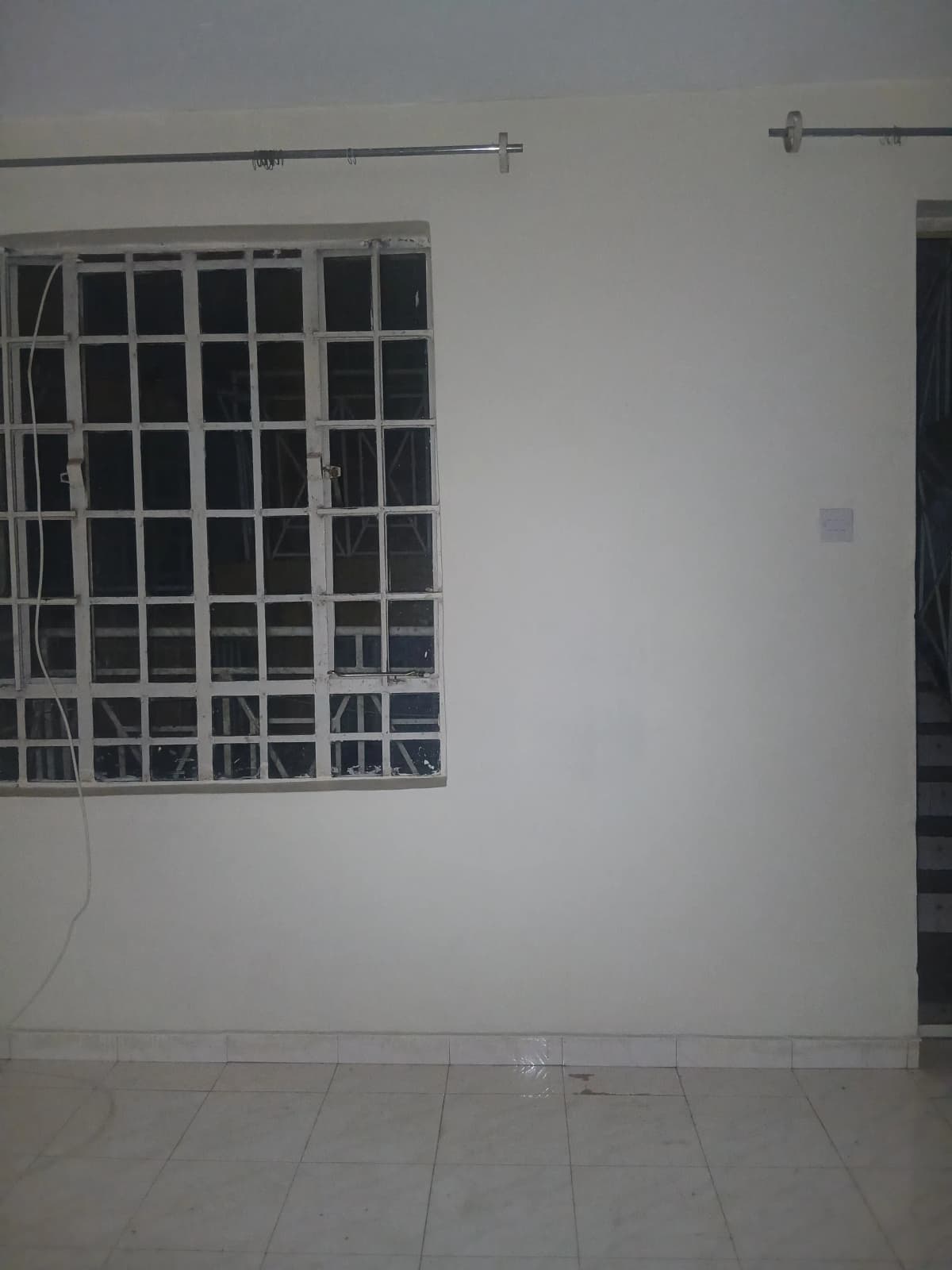 Empty bedroom with barred window and tiled flooring