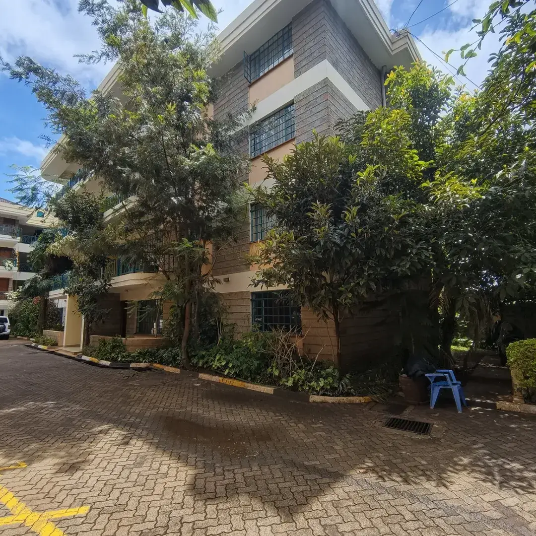 Multi-story residential building with mature landscaping and brick driveway.