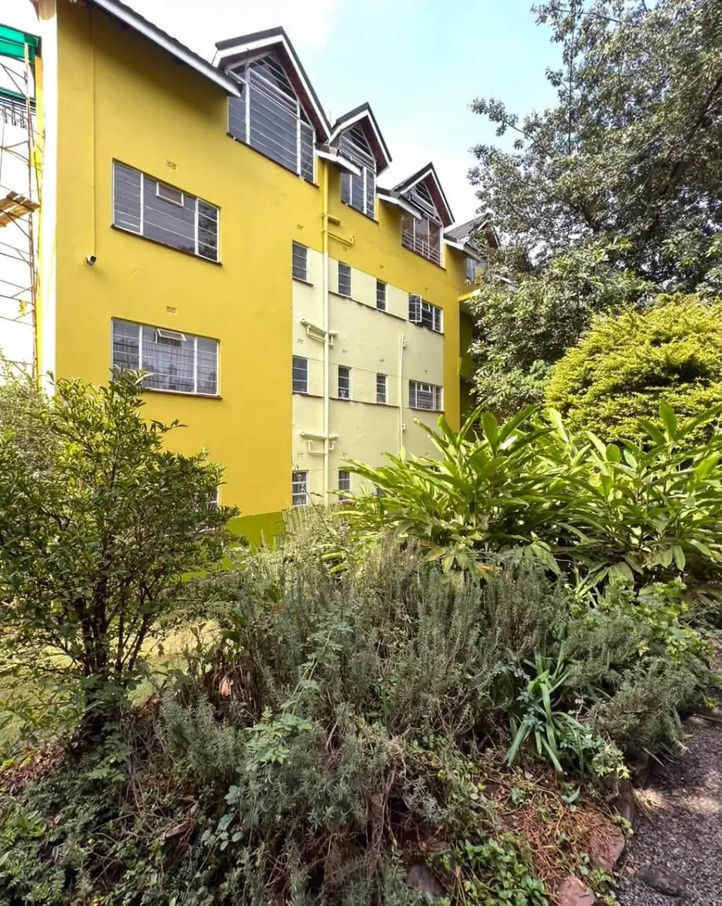 Bright yellow multi-story residential building with lush garden grounds