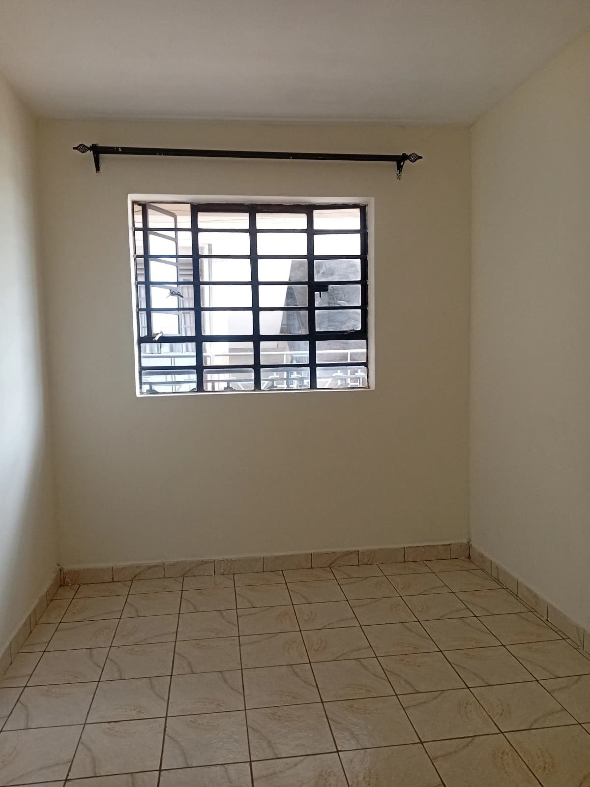 Empty bedroom with barred window and tiled flooring