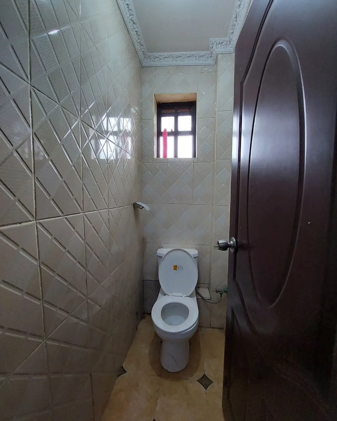 Compact toilet room with geometric tile walls and window