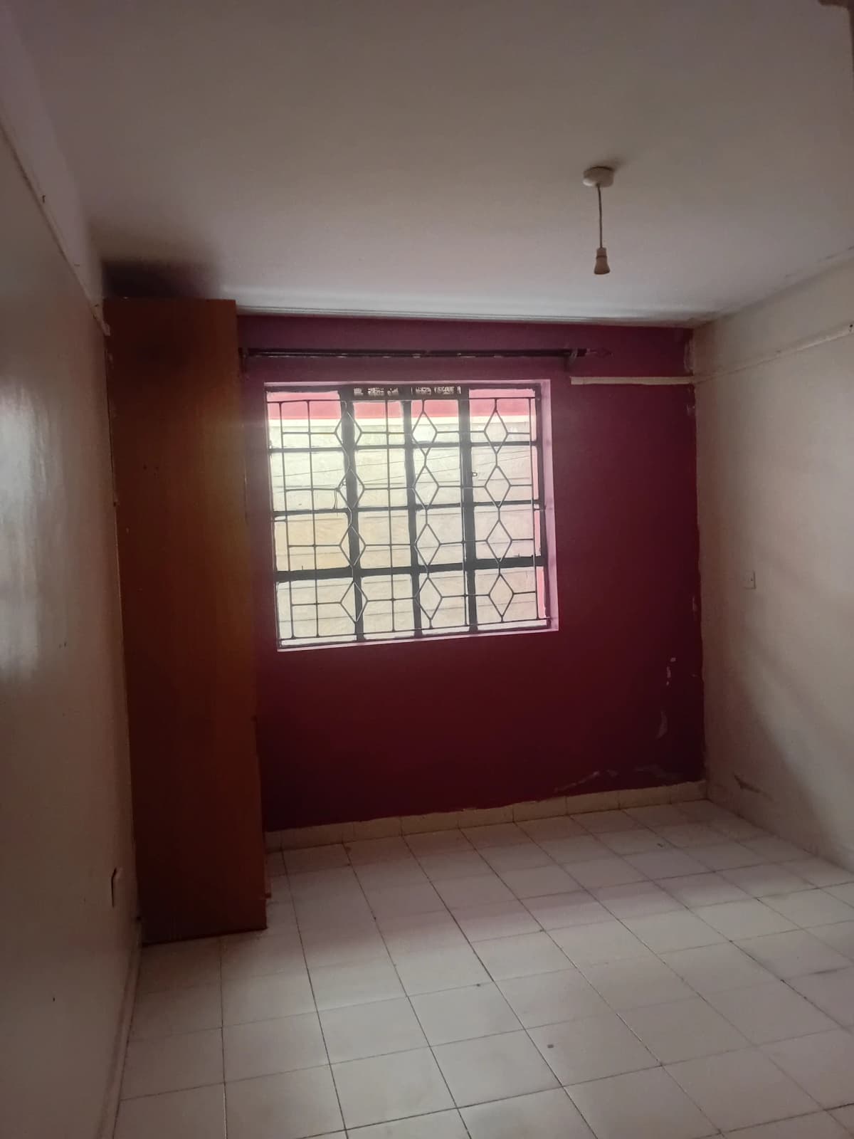 Empty living room with burgundy accent wall and barred window