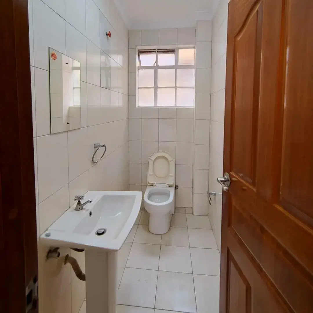 Clean bathroom with white tiles, sink, toilet, and natural window light