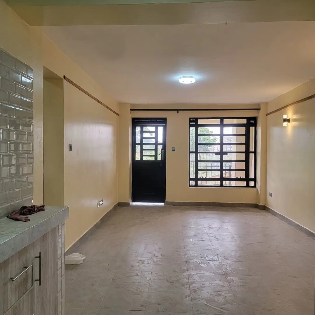 Open-plan living area with kitchenette, tiled flooring, entry door
