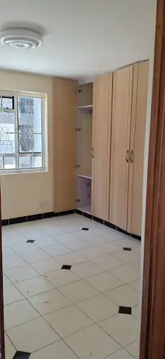 Spacious bedroom with built-in wooden wardrobes and tiled flooring