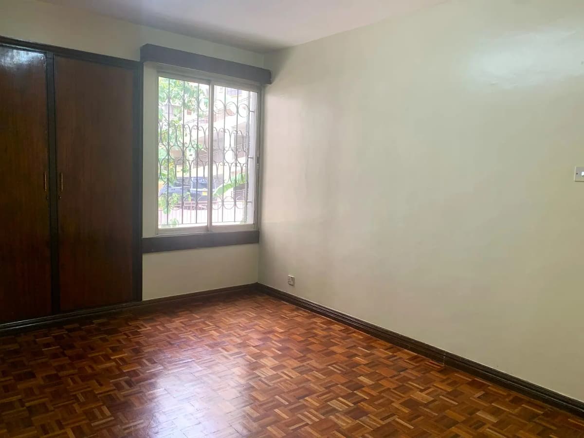 Spacious bedroom with herringbone wood flooring and barred window