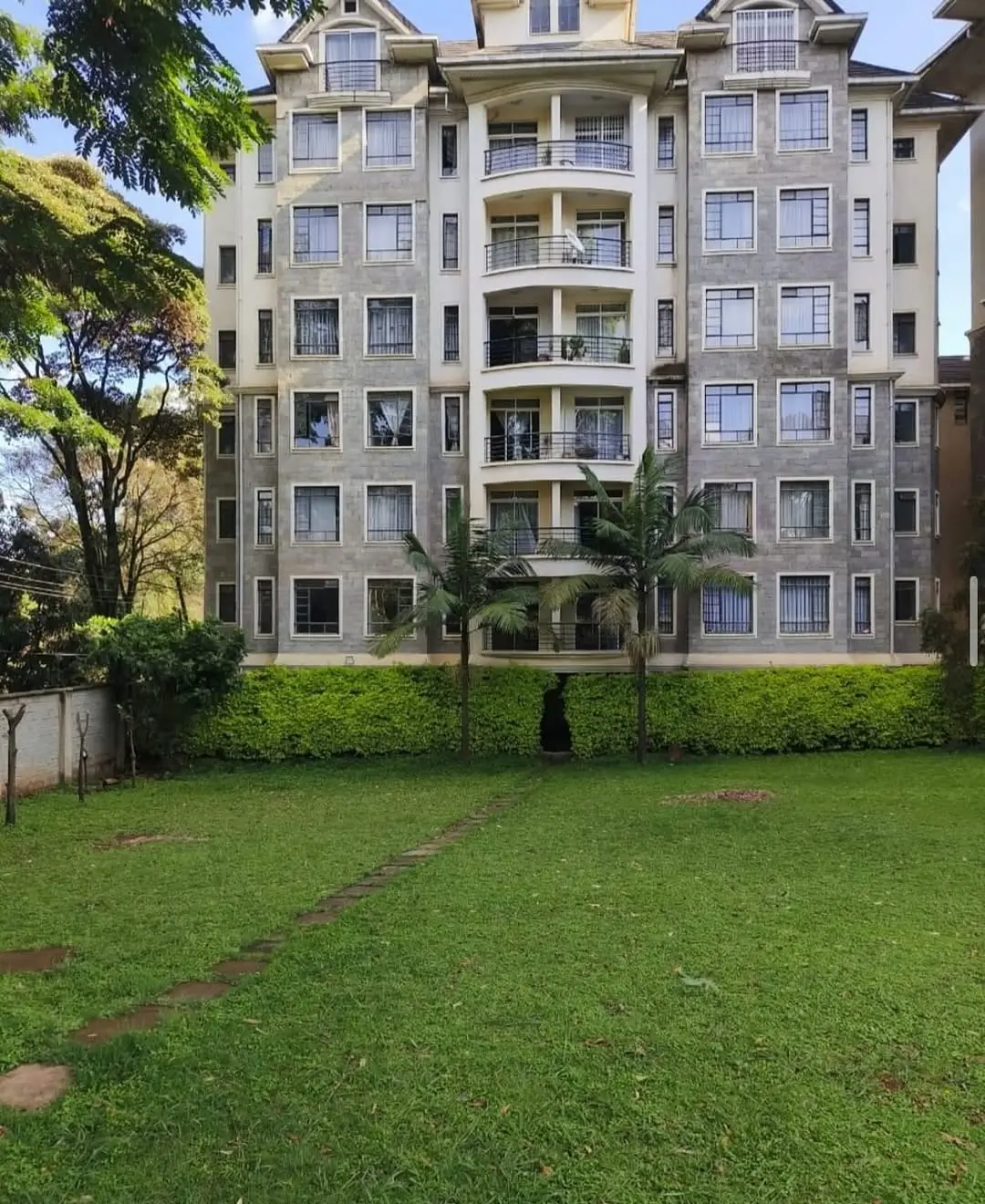 Multi-story residential building with manicured lawn and mature trees