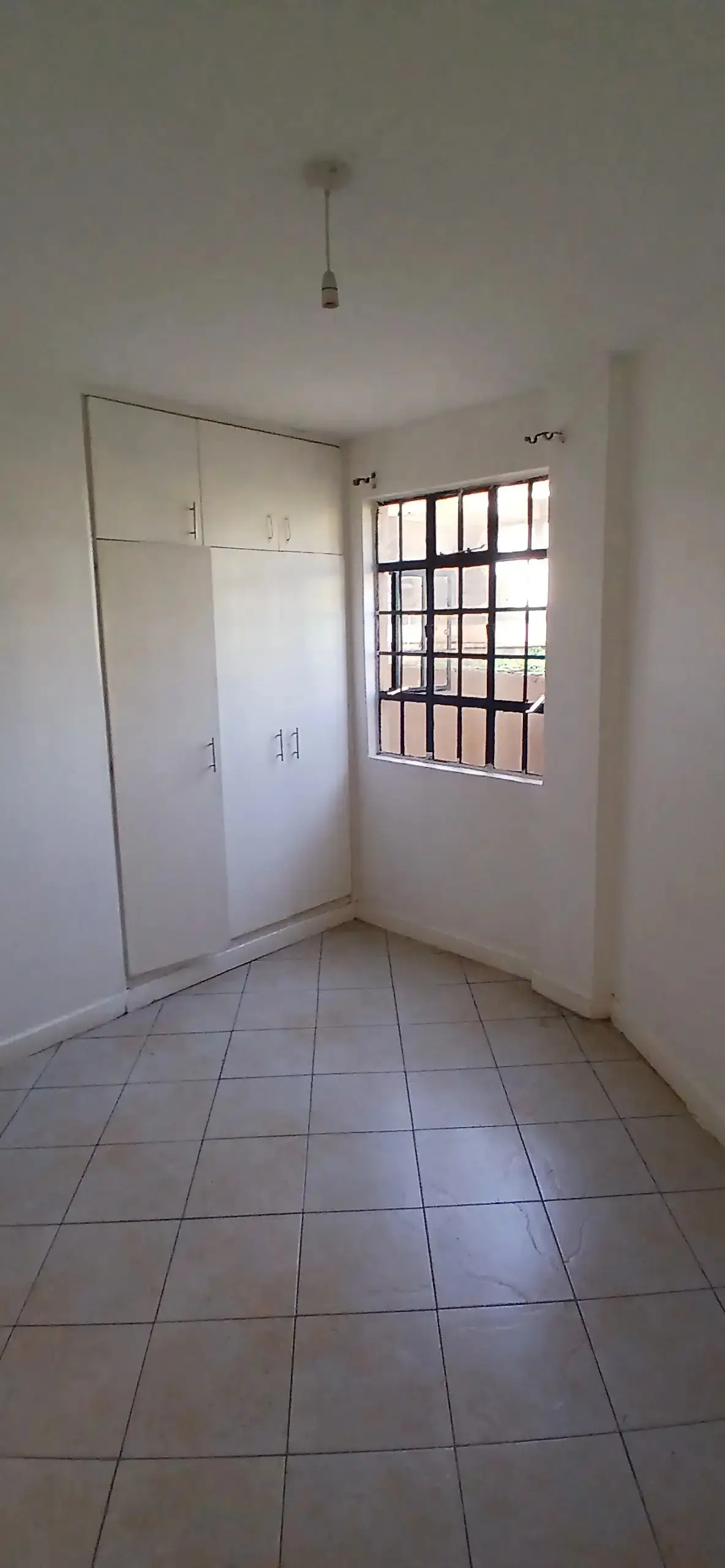 Bright empty bedroom with built-in wardrobes and barred window