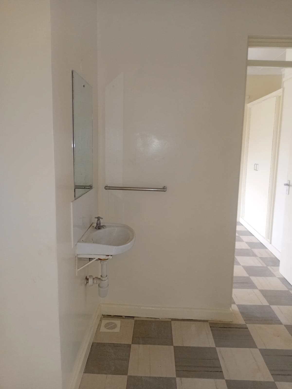 Compact bathroom with sink, mirror, and checkered tile flooring