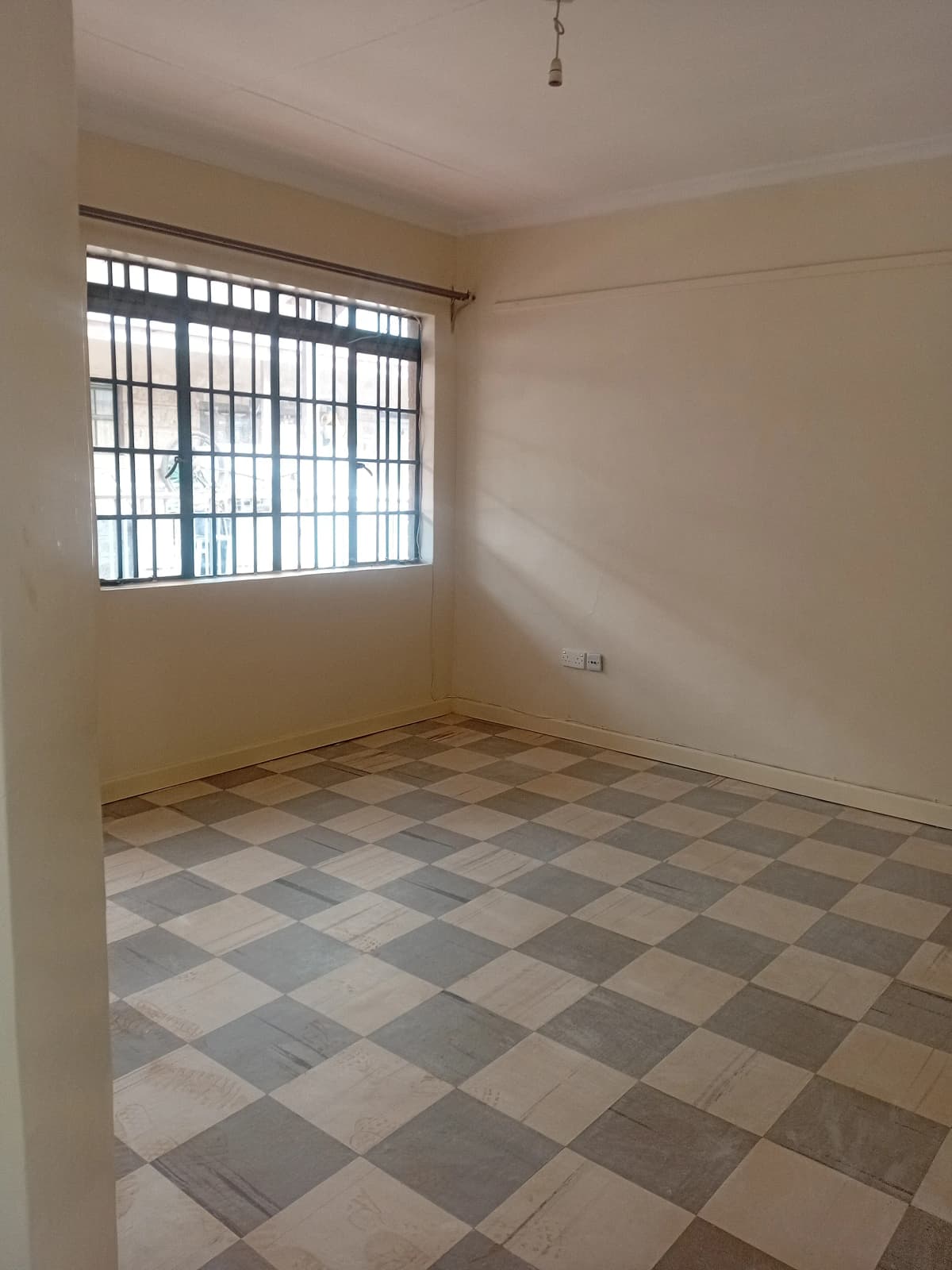 Empty bedroom with checkered tile floor and barred window