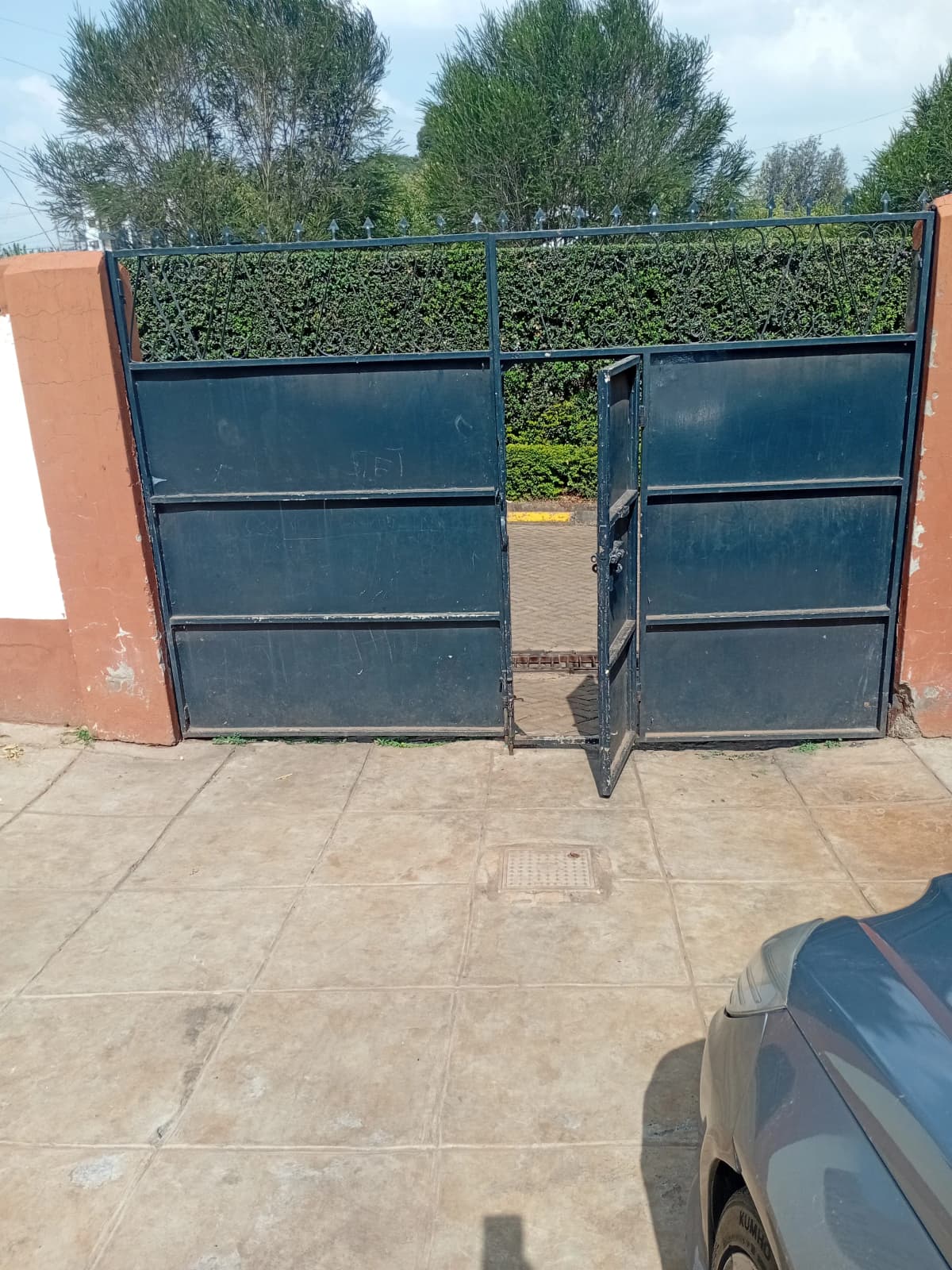 Compound entrance with blue metal gates and hedge fencing