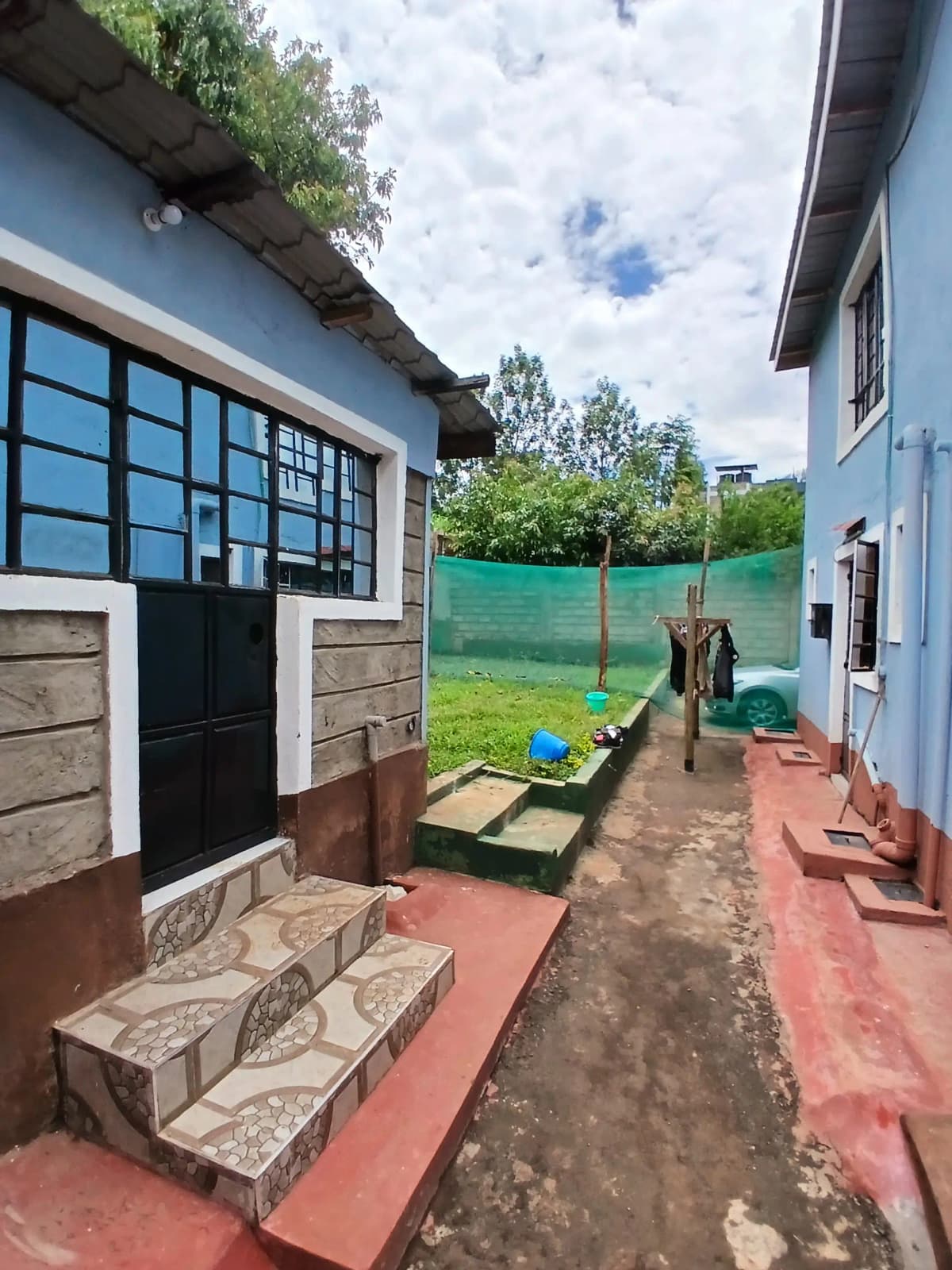 Compound entrance with blue-painted house facade and gated driveway