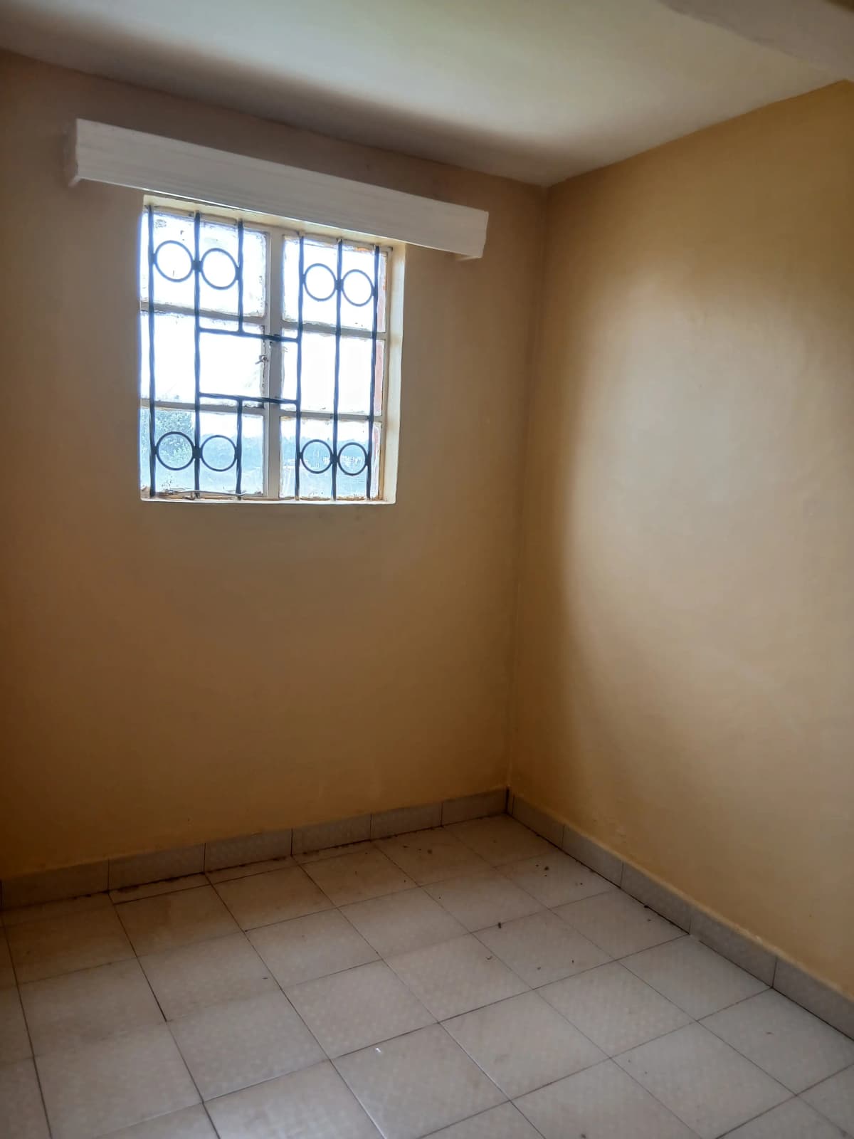 Empty bedroom with barred window and tiled flooring