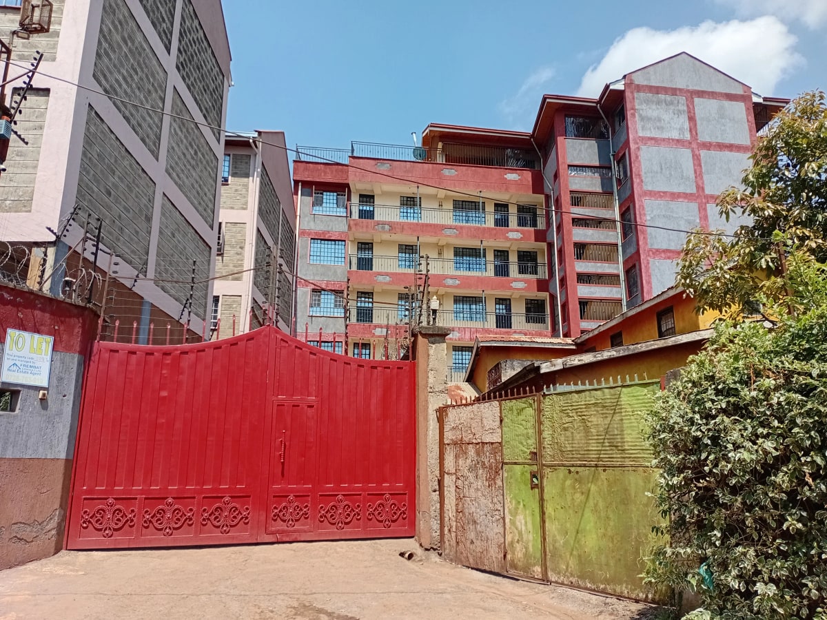 Compound entrance with red gate and multi-story apartment buildings