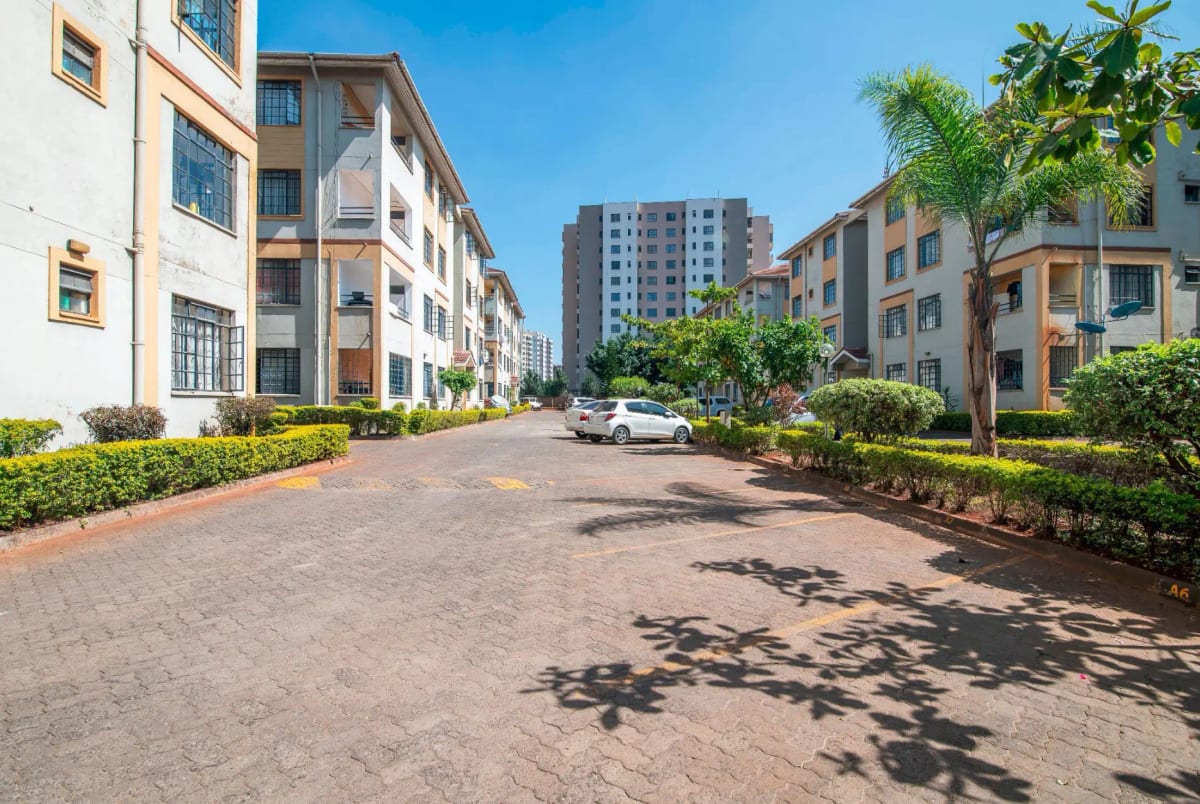 Residential compound driveway with manicured landscaping and multi-story buildings