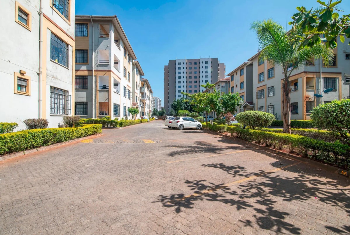 Residential compound driveway with manicured landscaping and multi-story buildings