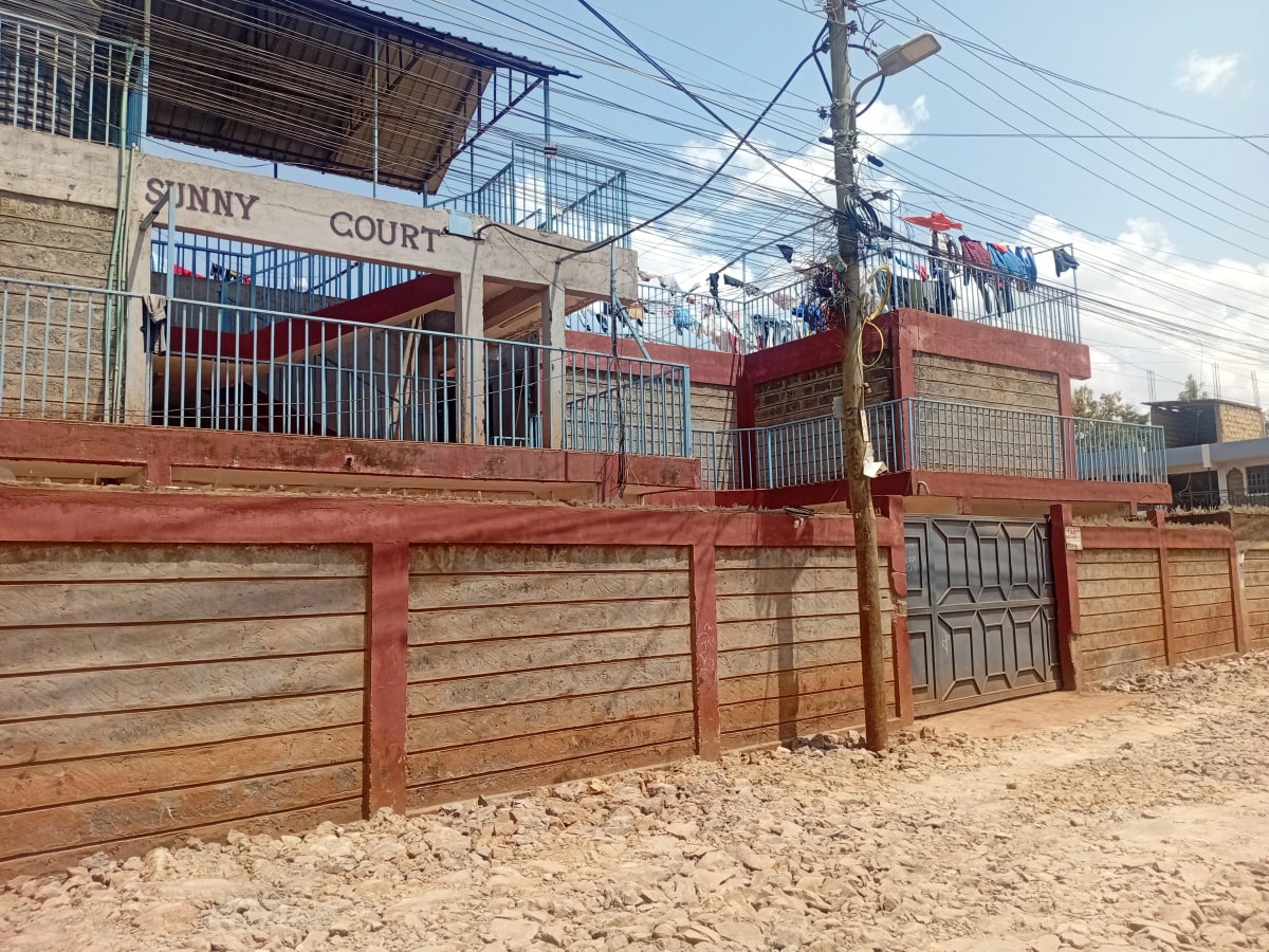 Red brick residential building with wooden gates and compound walls