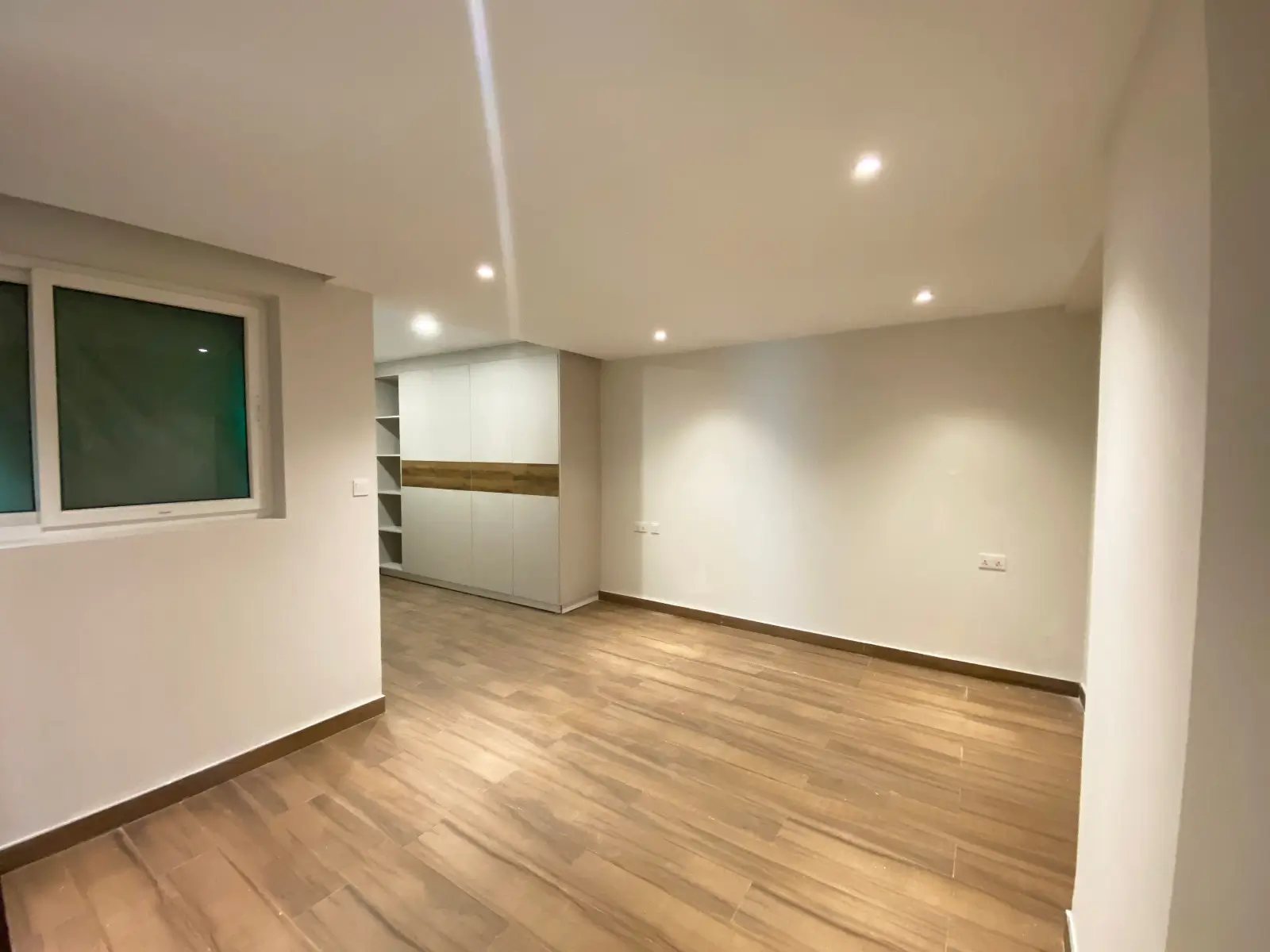 Spacious open-plan living area with wooden flooring and built-in shelving