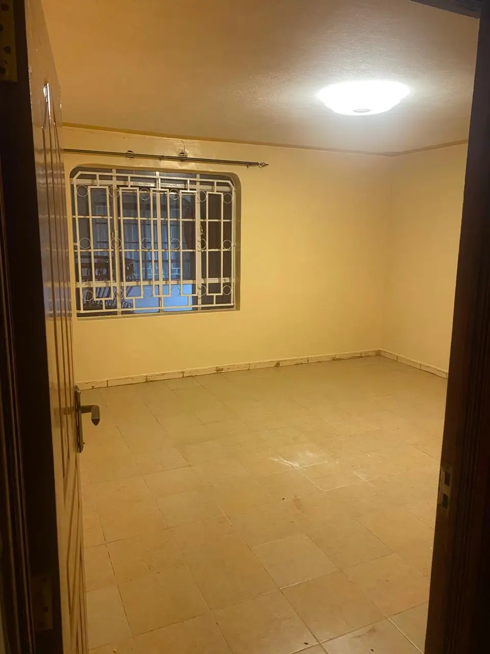 Spacious empty bedroom with barred window and tiled floor