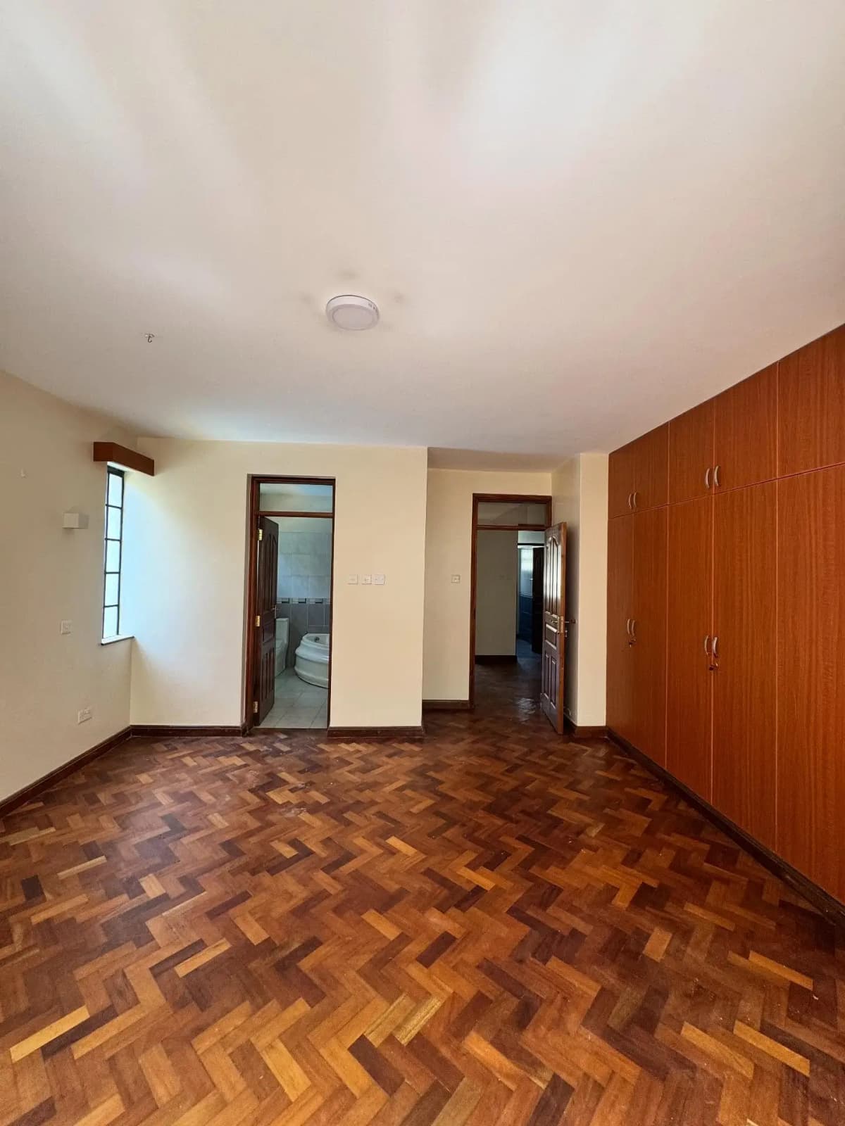 Spacious bedroom with herringbone wooden floor and built-in wardrobes