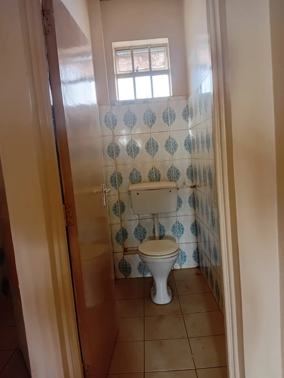 Compact toilet with leaf-patterned tiles and window