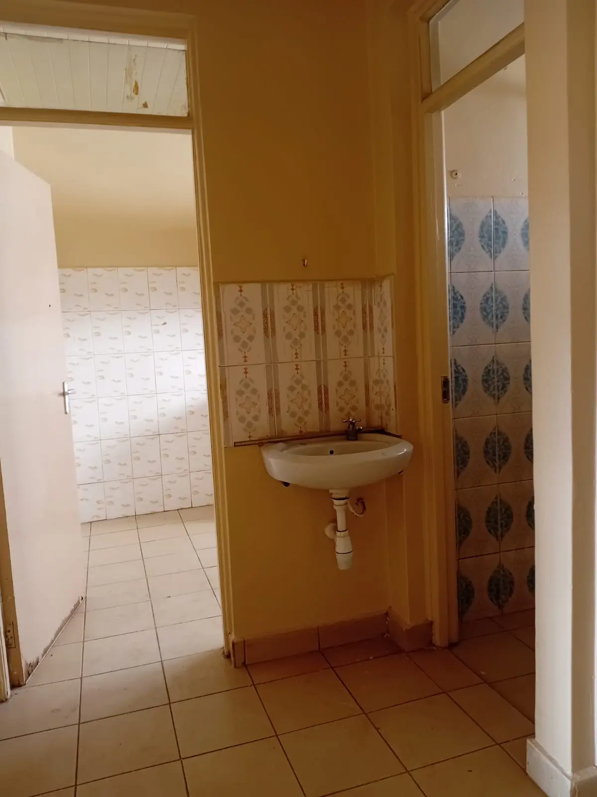 Bathroom with pedestal sink and tiled walls, adjacent shower area visible