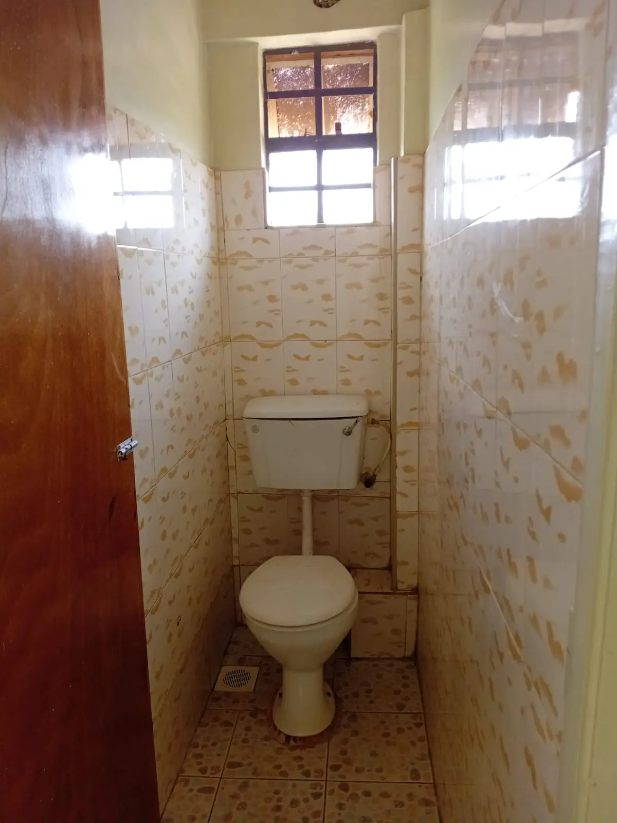 Compact toilet room with beige patterned tiles and window
