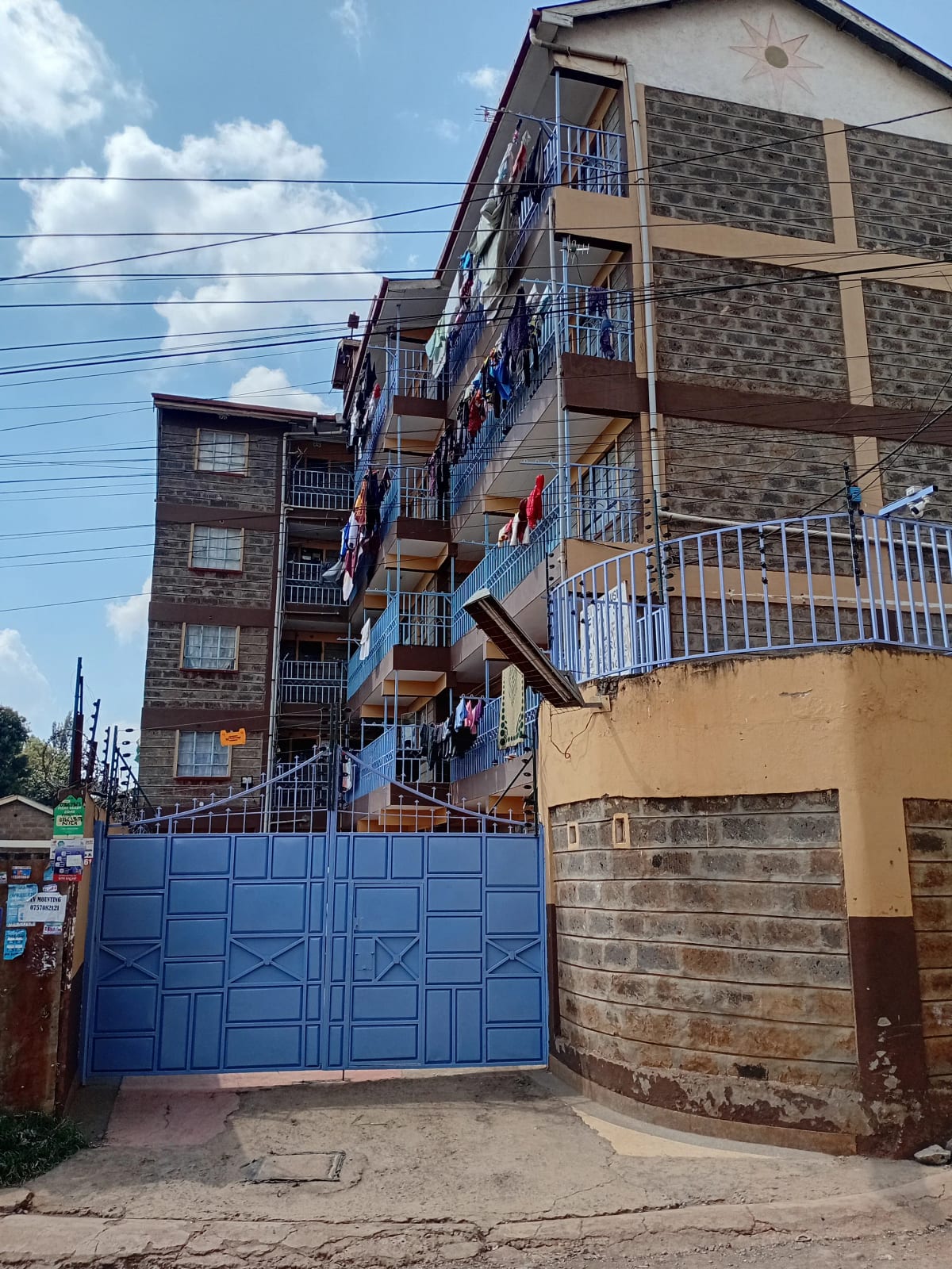 Multi-story residential building with blue gate and compound entrance