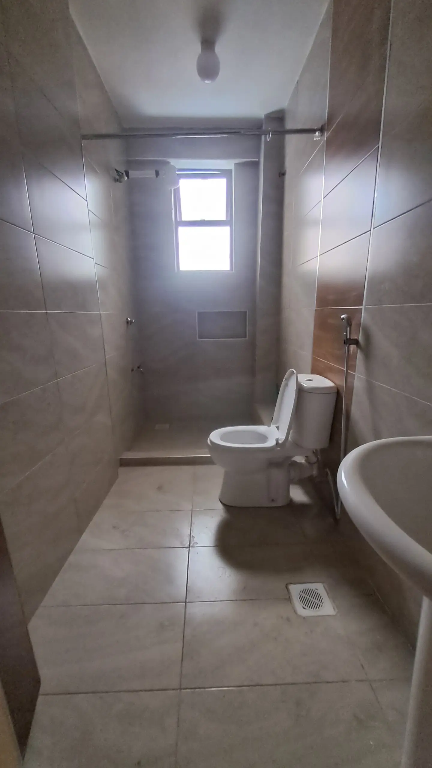 Narrow bathroom with toilet, sink, and shower enclosure