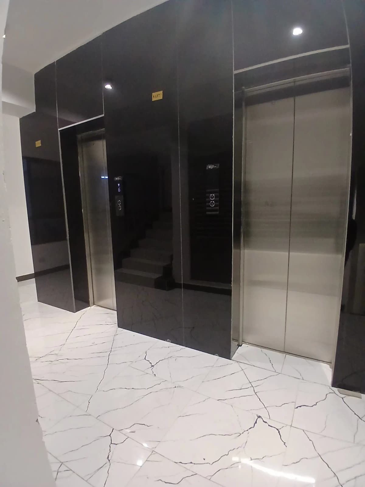 Modern lobby with dual elevators, black paneling, marble flooring